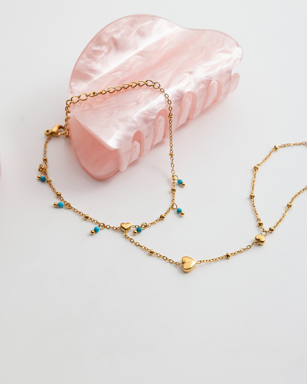 Gold necklace with heart-shaped pendants on a pink stone background