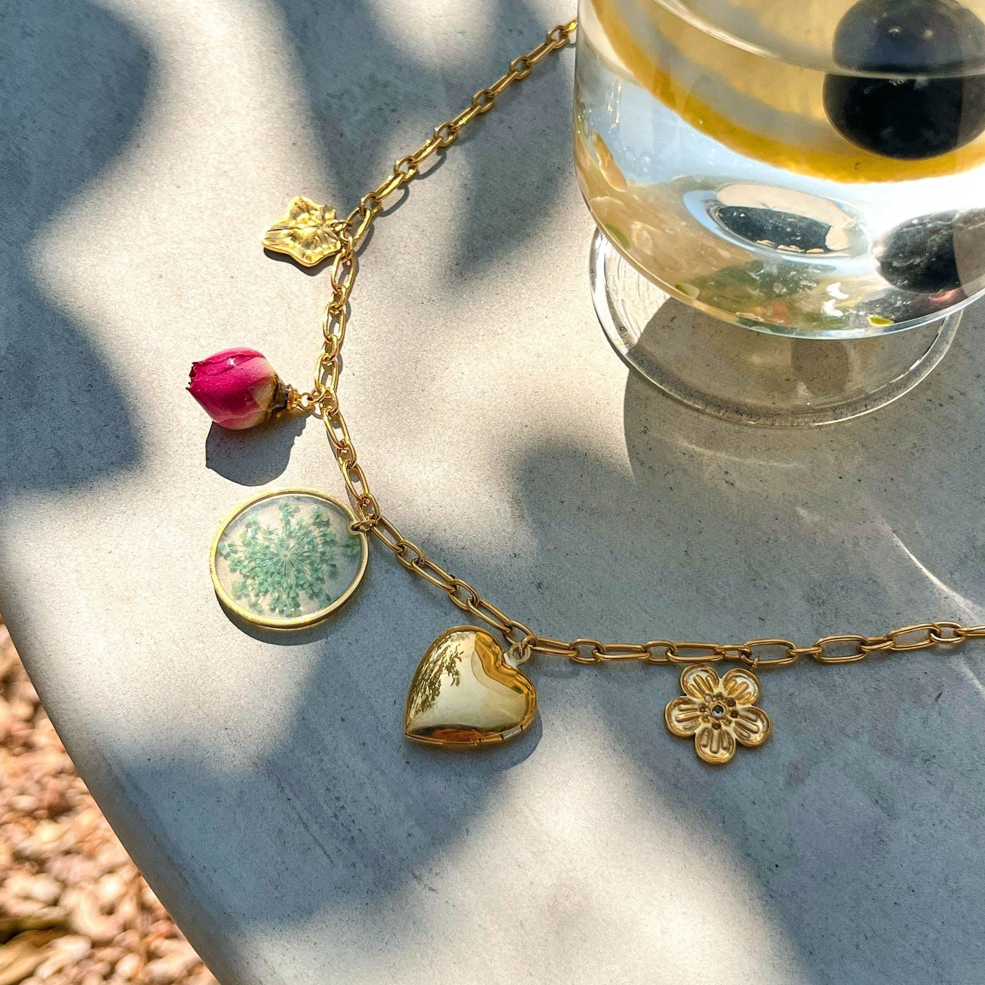 Collection of gold charm necklaces with rose, floral, and heart pendants on outdoor table