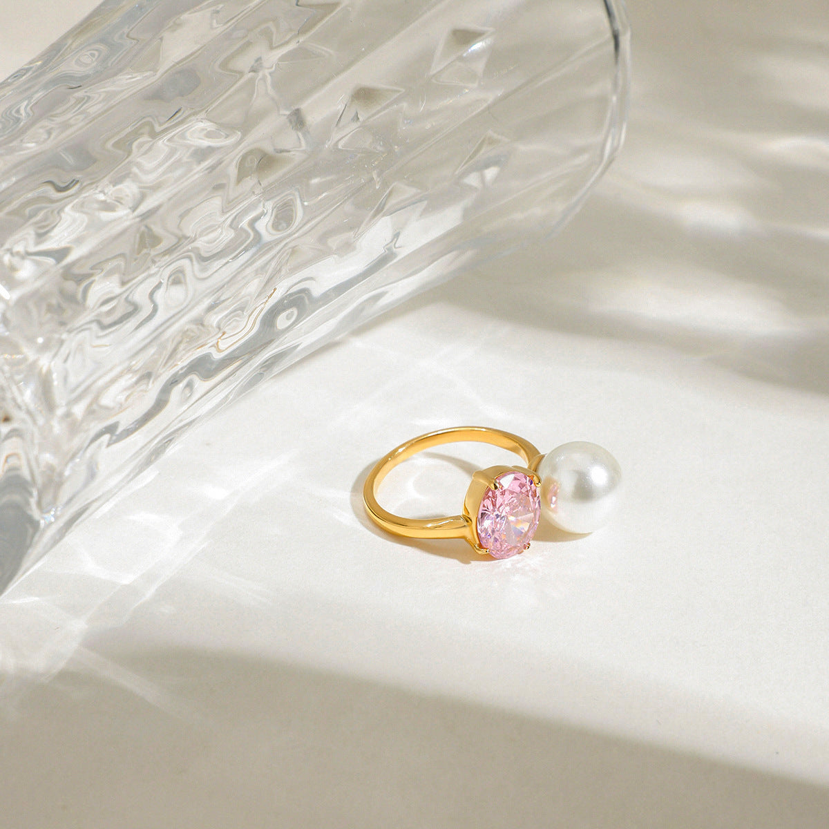 Detailed view of gold ring featuring pearl and pink zirconia on white surface