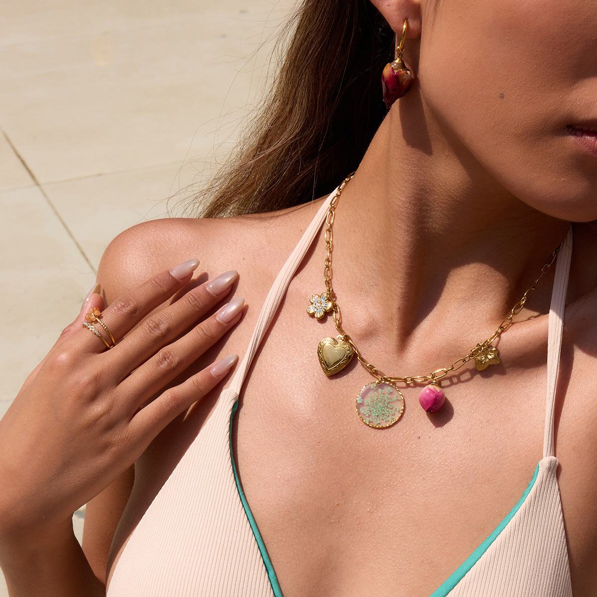 Close-up of model wearing a gold chain necklace with heart locket and rosebud pendant by the pool