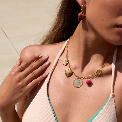 Close-up of model wearing a gold chain necklace with heart locket and rosebud pendant by the pool
