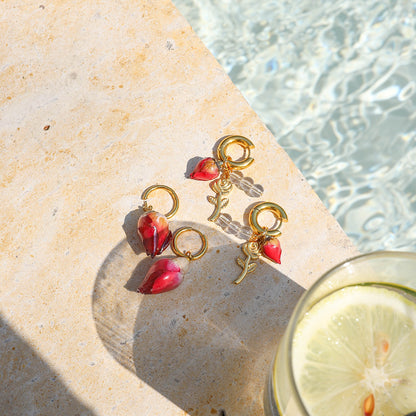 Pair of gold hoop earrings with preserved rosebuds and charms by a sunlit pool