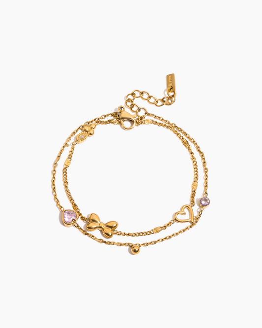 Gold bracelet with heart and bow designs on a white background