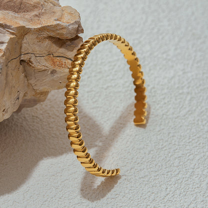 Curved open gold bracelet featuring ribbed beaded finish, placed vertically on stone