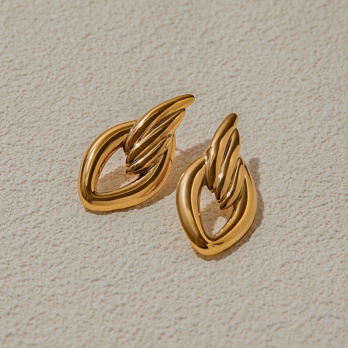 Chunky gold twisted earrings on beige textured background