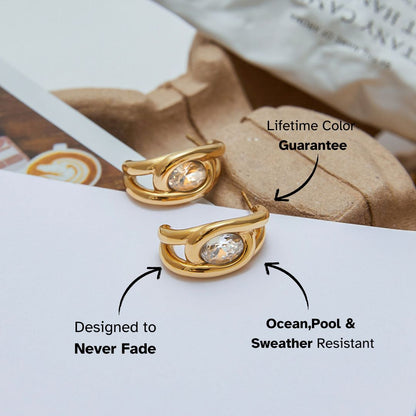 Close-up of sculpted gold oval crystal earrings resting on minimal background