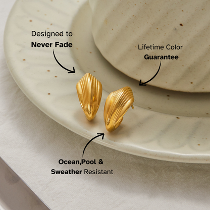 Minimal gold wave-shaped stud earrings on ceramic plate