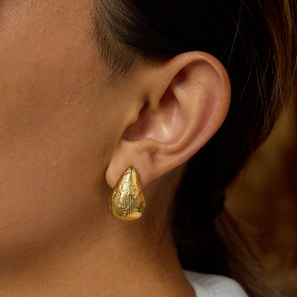 Model wearing bold gold nugget earrings with white shirt