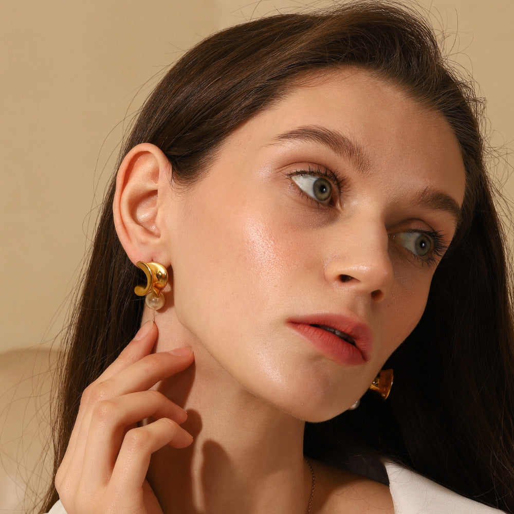 Gold sculpted pearl earrings with modern wave design on model