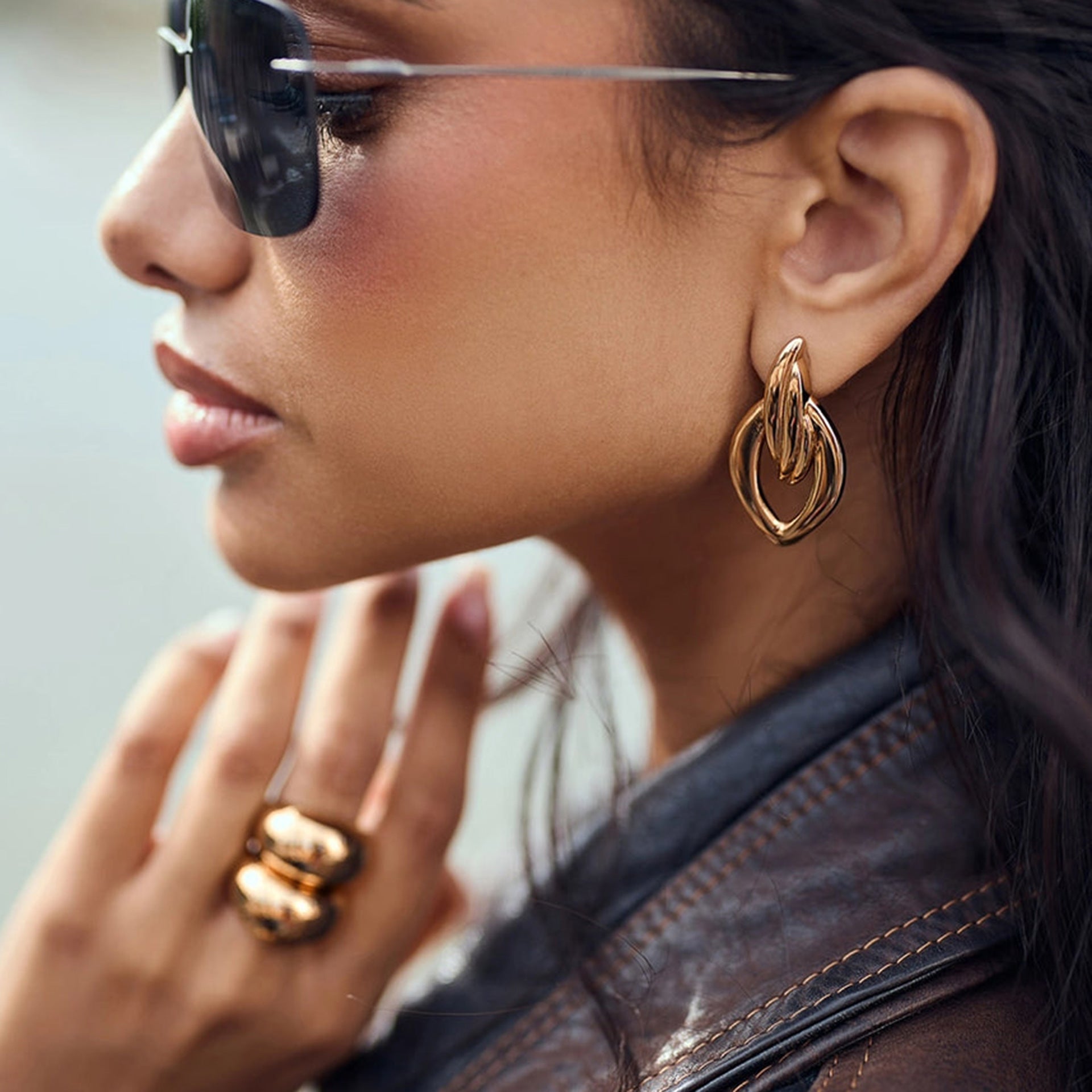 Model wearing bold sculptural gold earrings with sunglasses