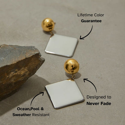 Minimalist metallic drop earrings laid on neutral concrete