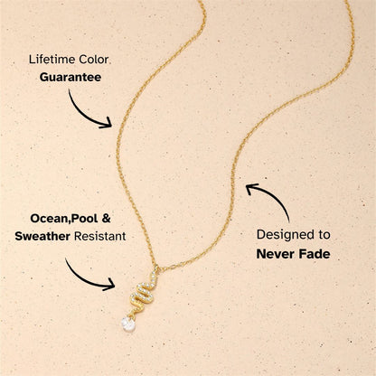 Snake pendant gold necklace with crystal drop, flat lay on creamy stone background