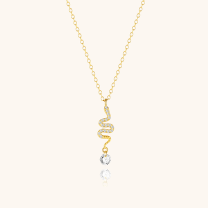 Gold twisted snake necklace with crystal drop laid on beige background, delicate and stylish