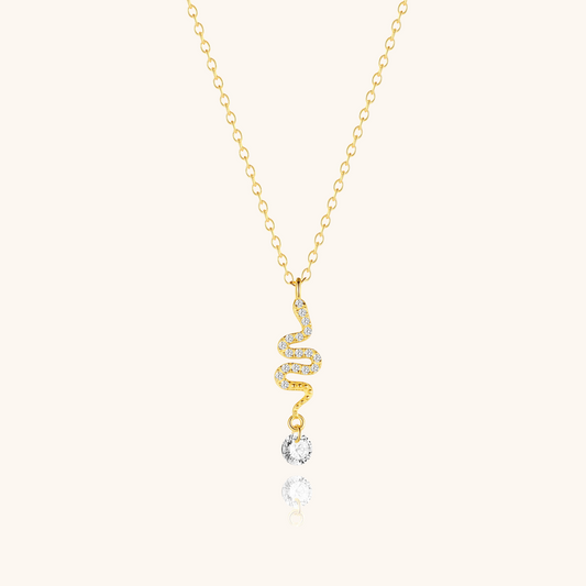 Gold twisted snake necklace with crystal drop laid on beige background, delicate and stylish