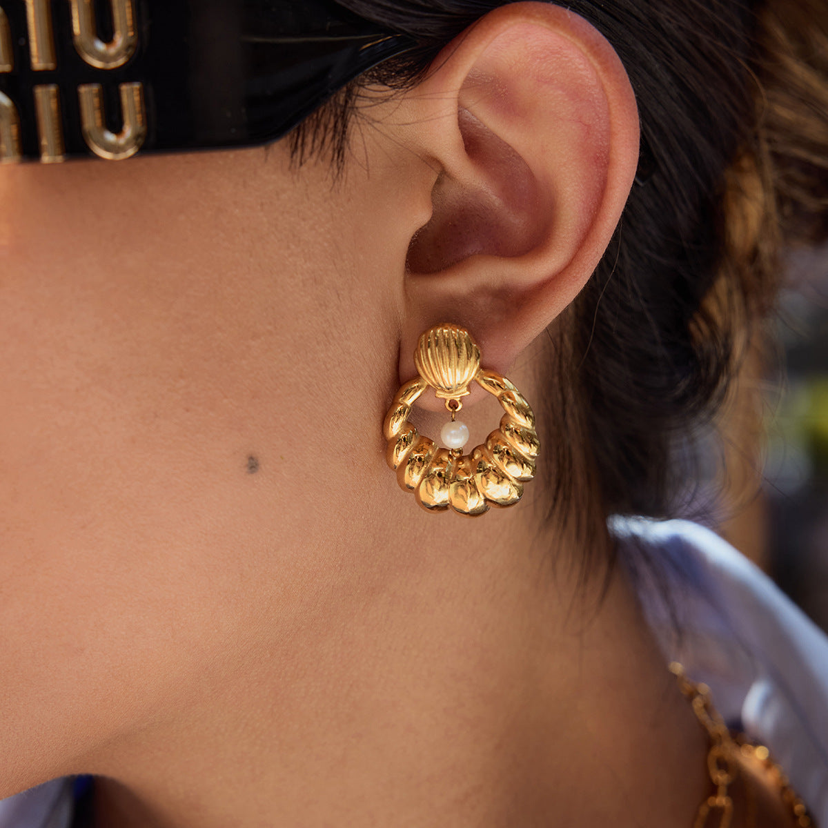 Close-up of model wearing shell pearl earrings with gold finish