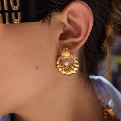Close-up of model wearing shell pearl earrings with gold finish