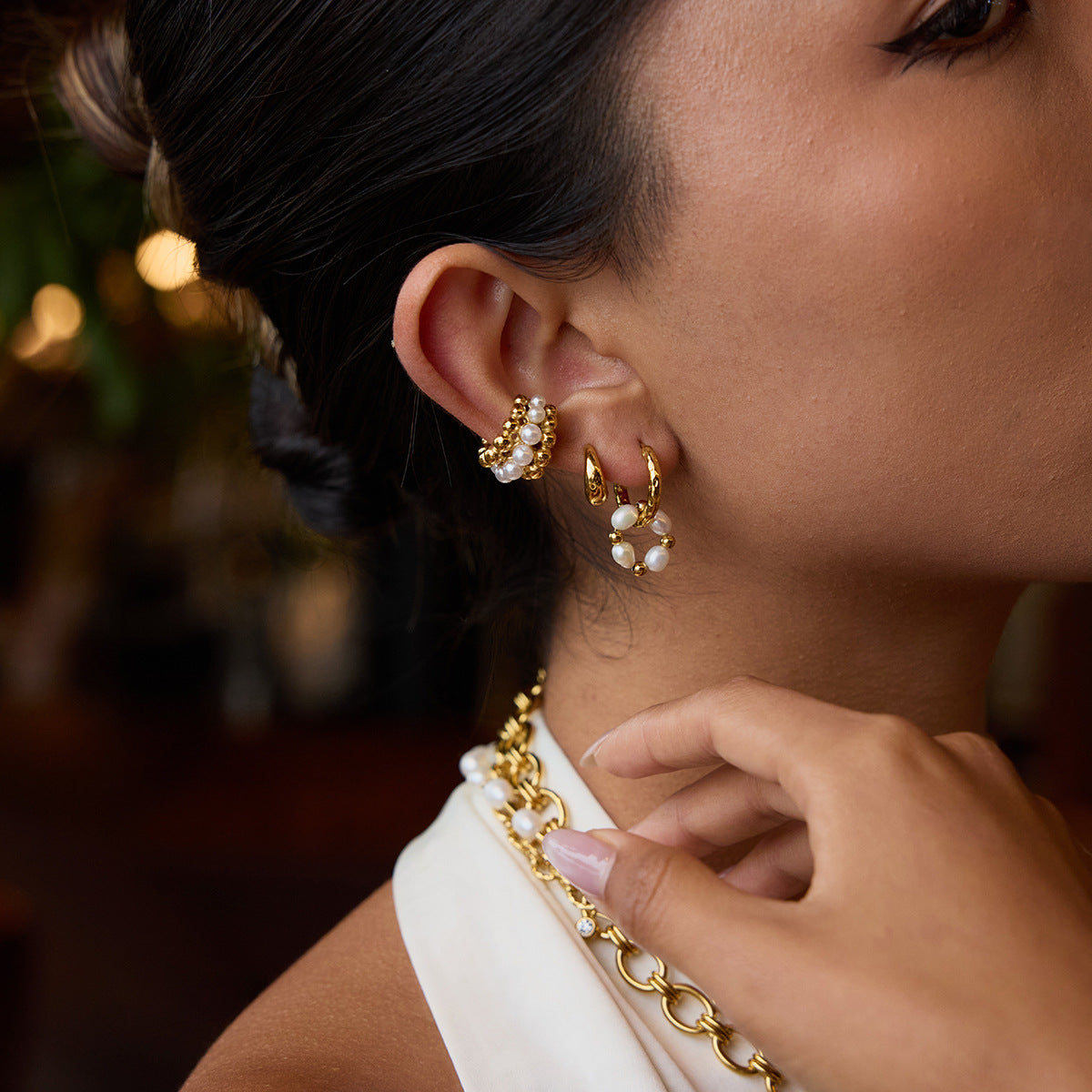 Chic side view of a woman styling gold hammered hoops with pearls, paired with a statement pearl necklace.