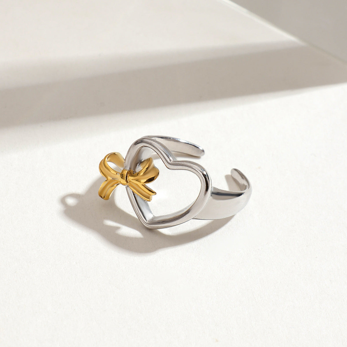 Minimalist shot of heart-shaped ring with golden bow resting on a clean white surface.