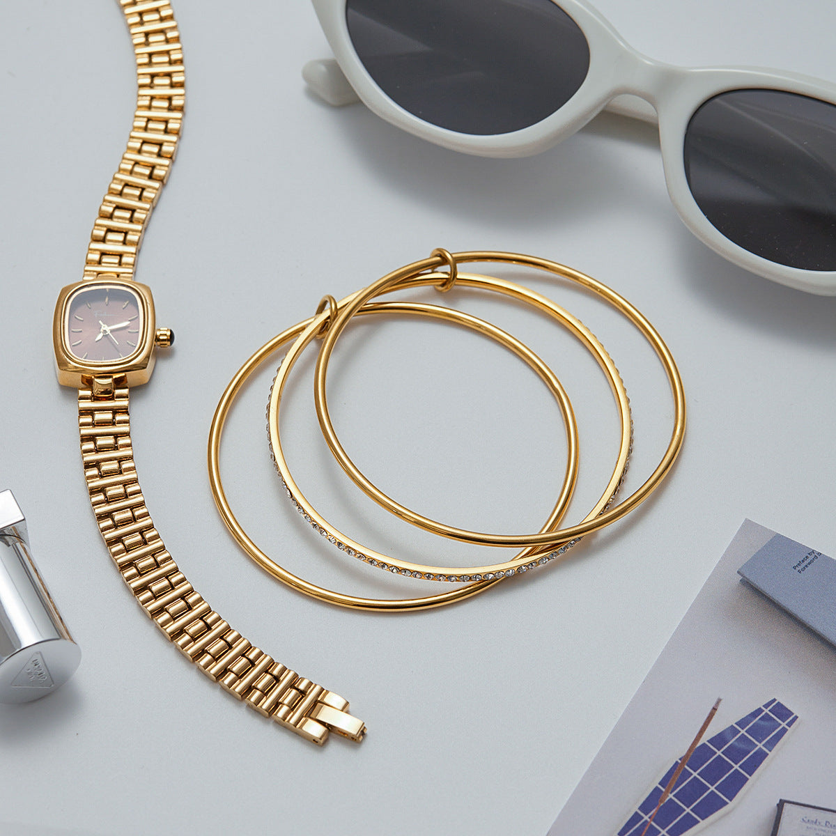 Gold stacking bangles styled with watch and sunglasses on flatlay
