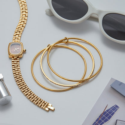 Gold stacking bangles styled with watch and sunglasses on flatlay