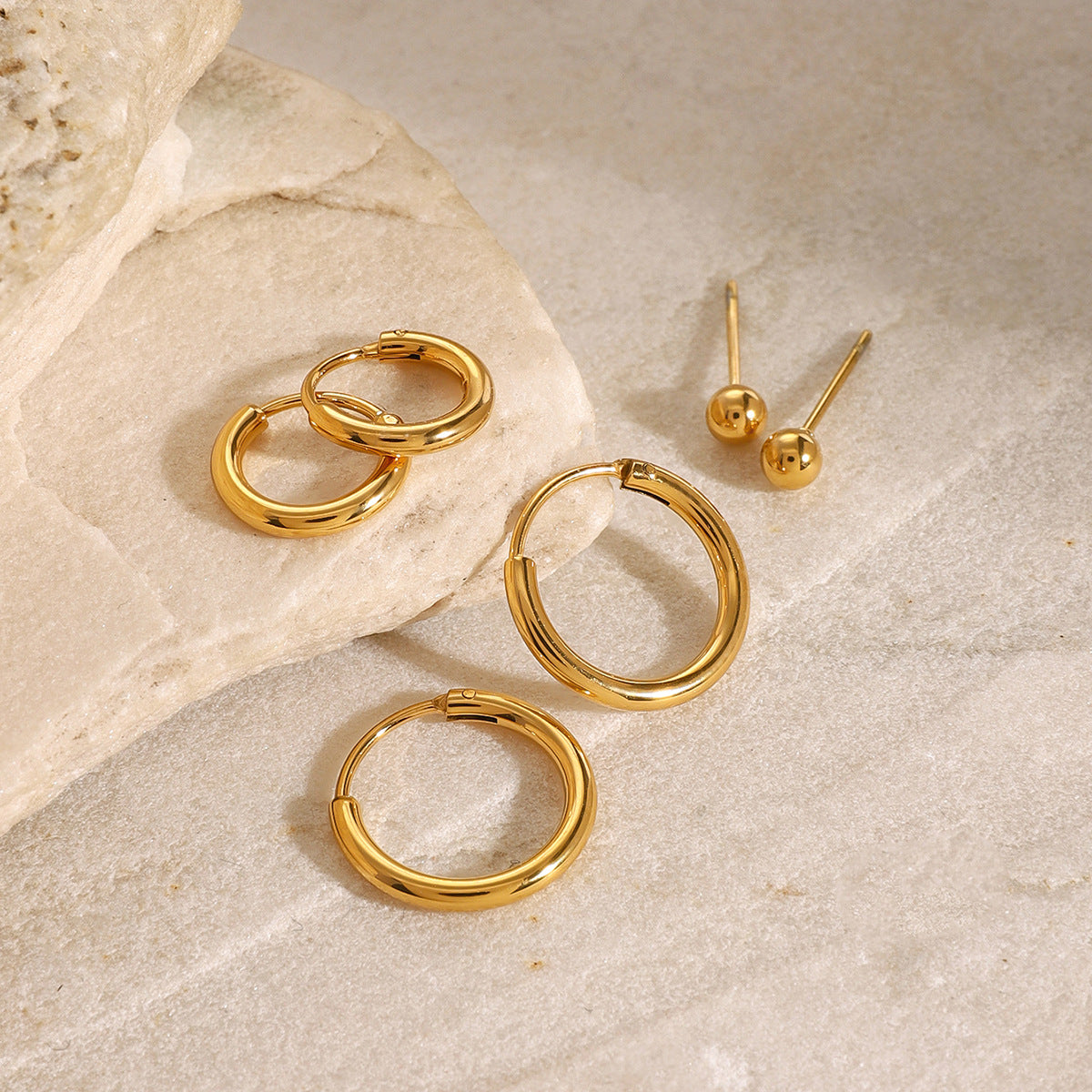 Gold hoop earrings set displayed on stone background, minimalist aesthetic