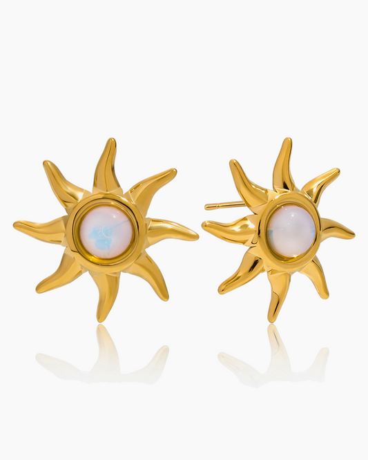Gold sun-shaped earrings with a central gemstone on a white background