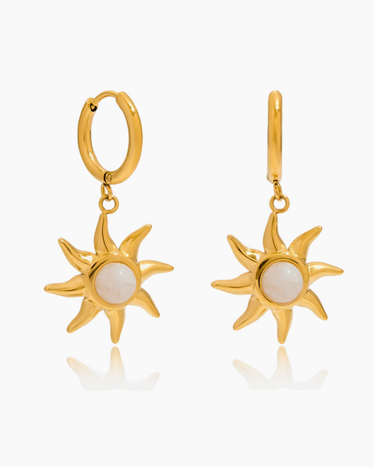 Gold sun-shaped earrings with a white center on a white background