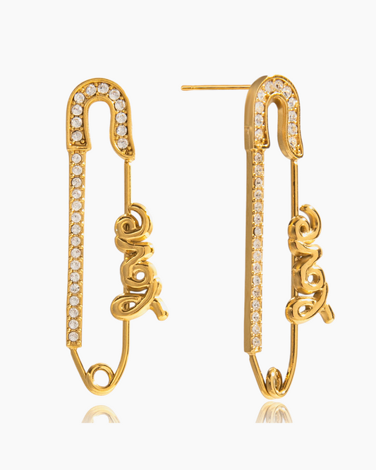 Close-up of a single gold safety pin earring adorned with sparkling crystals and the word "Love."
