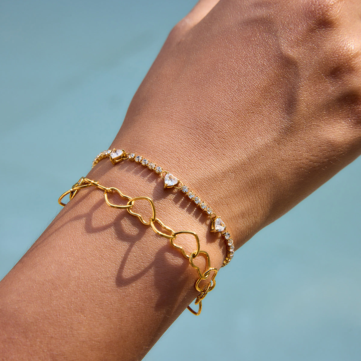 Gold heart chain bracelet stacked with zircon heart tennis bracelet on model wrist