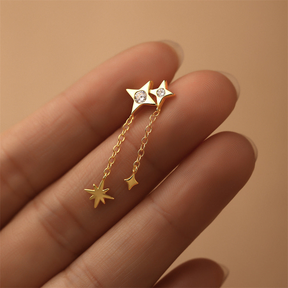 Dainty rhinestone earring with dangling star, shown close-up on hand.