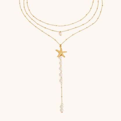 Close-up of starfish pendant and pearl strand layered necklace on neutral background