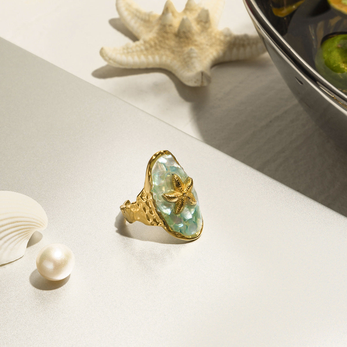Detailed product image of gold starfish ring with blue crushed shell resin on white background