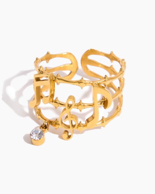 Gold bracelet with musical notes and a clear gemstone on a white background