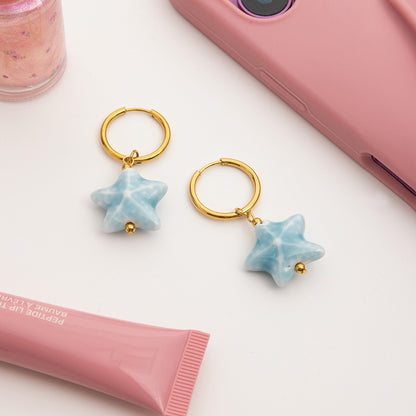 Star-shaped earrings with gold hooks on a white surface with pink phone and lip balm.