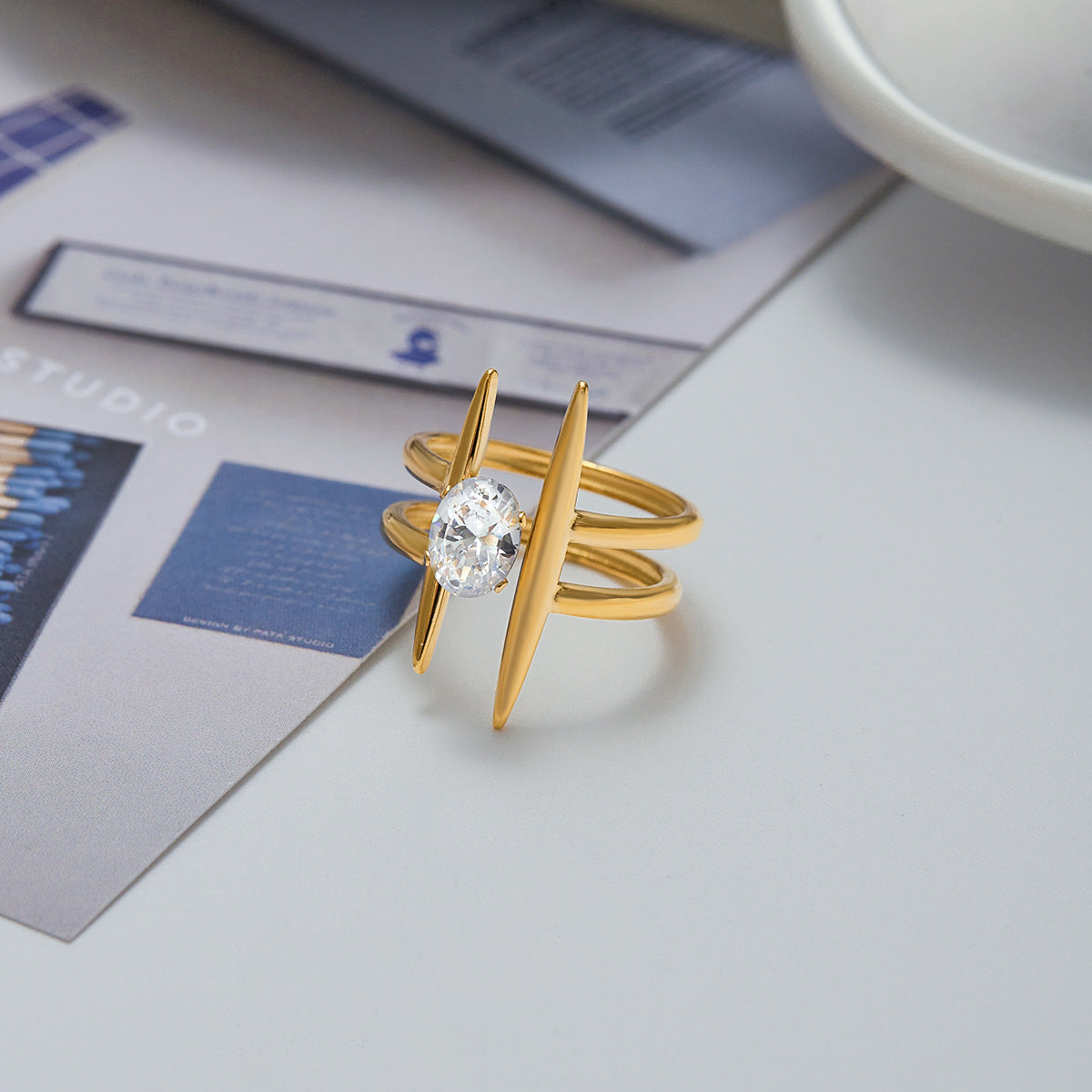 Stylish gold cocktail ring resting next to fashion sunglasses and magazine