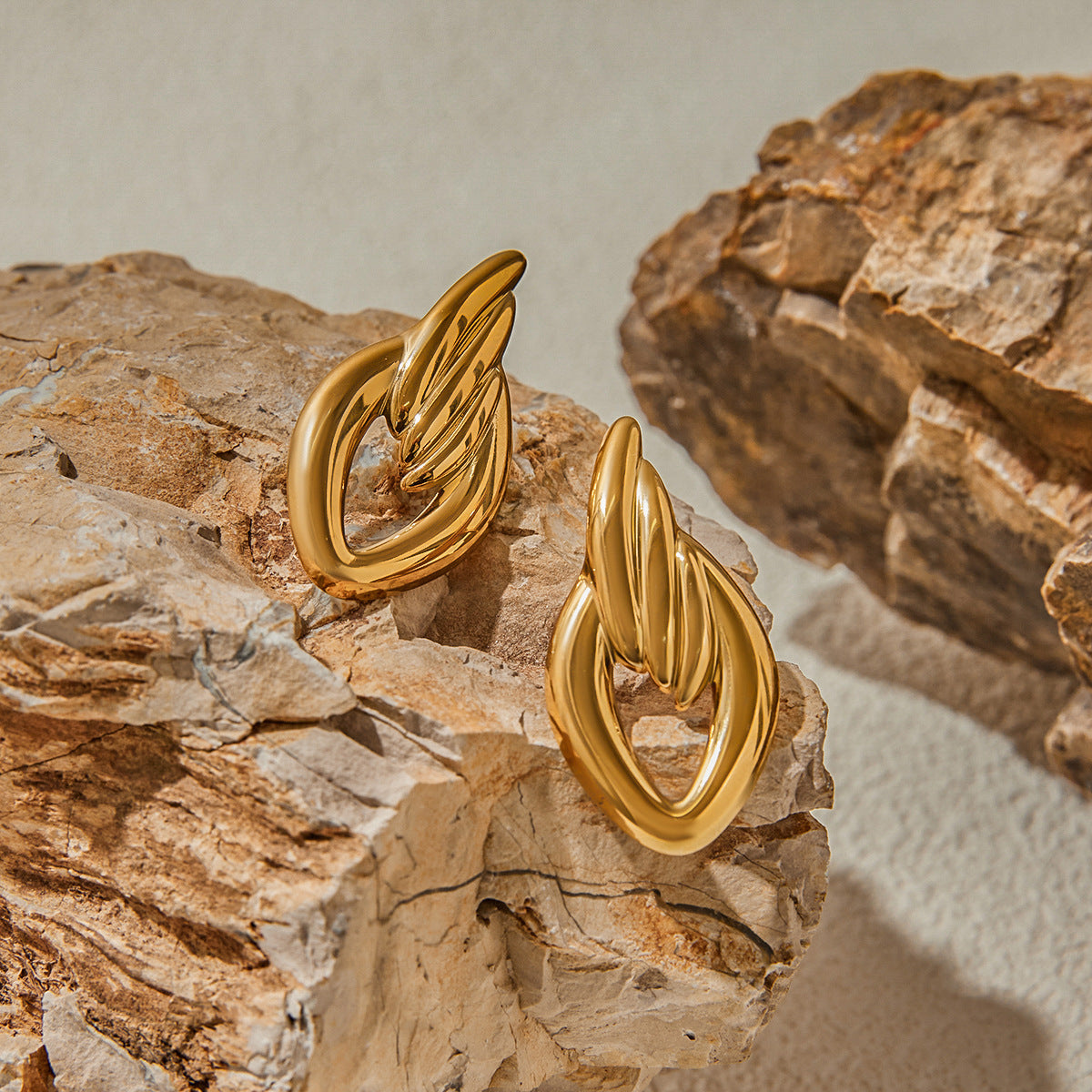 Bold gold sculptural earrings displayed on natural rock background