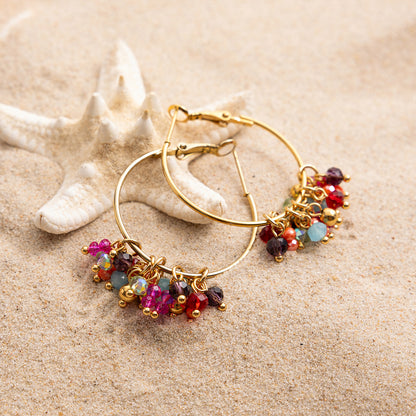 Gold hoop earrings with colorful beads on a sandy background