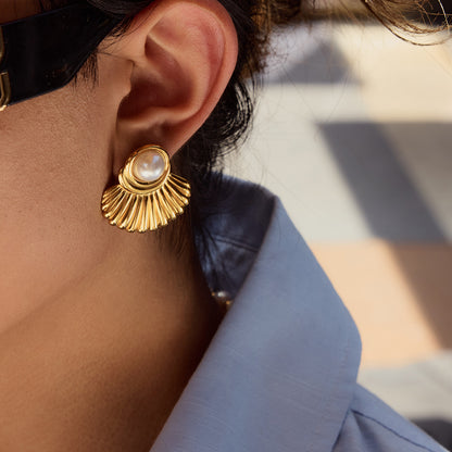 Woman wearing shell pearl earrings outdoors with sunlight.