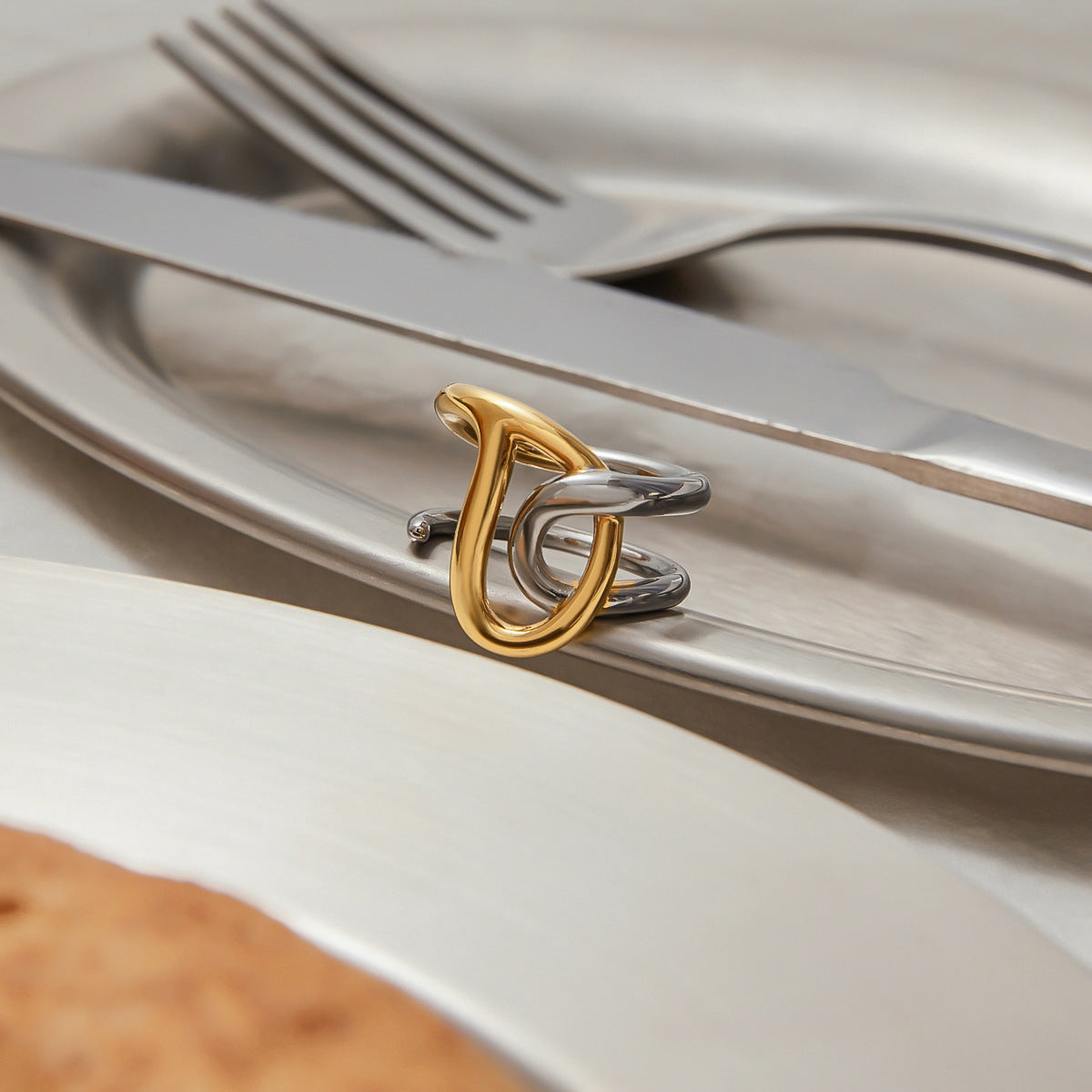Bold twisted gold-silver ring styled on silver dining setting with soft lighting