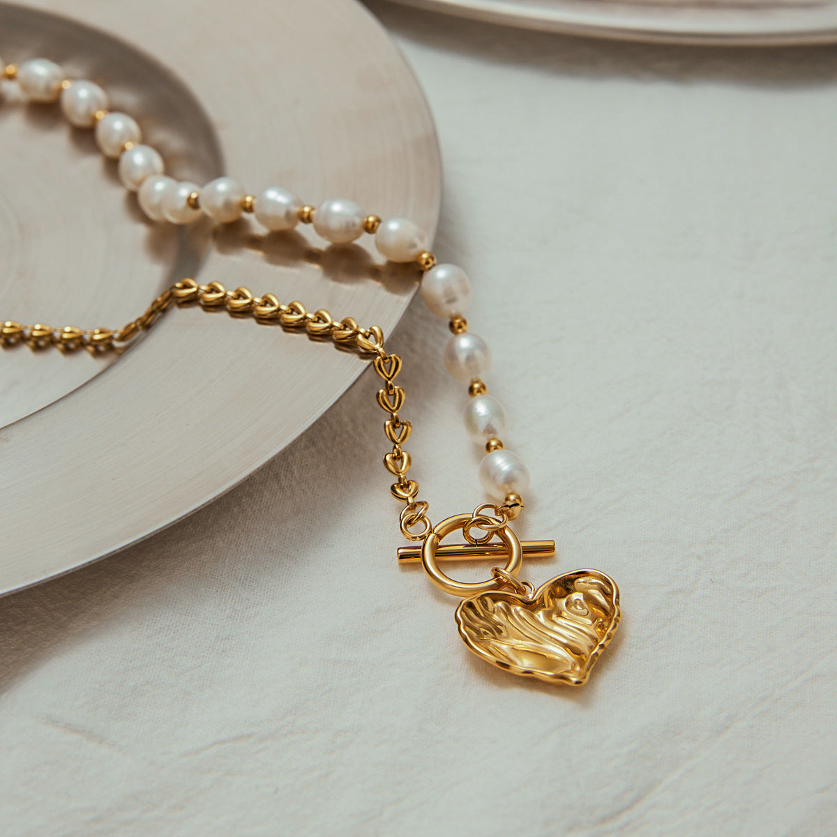 Minimalist background highlighting asymmetrical pearl and chain necklace with hammered gold heart charm