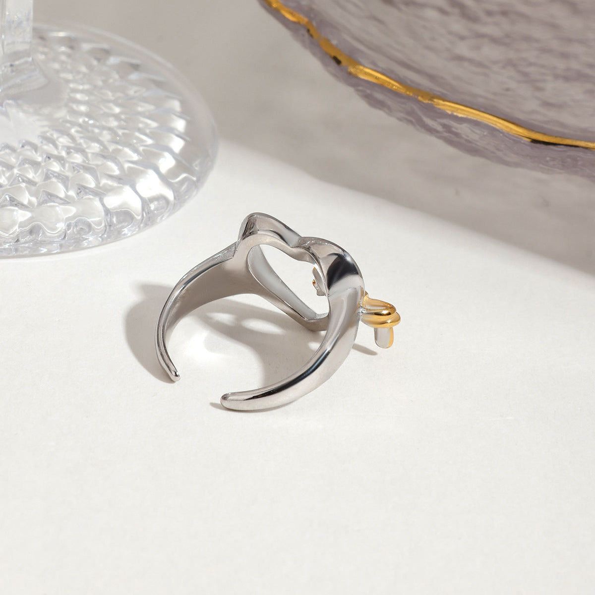 High-resolution product shot of silver heart open ring with gold bow on neutral background.