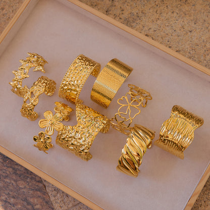 Assorted golden open cuff bracelets displayed in a tray with different textures and shapes