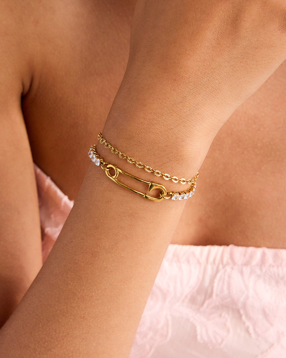 Elegant hand wearing summer jewelry stack featuring gold bracelet with safety pin and crystals