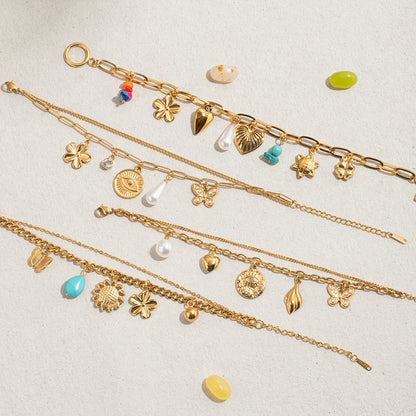 Colorful gold chain bracelet with heart and shell charms, styled flat on sandy surface