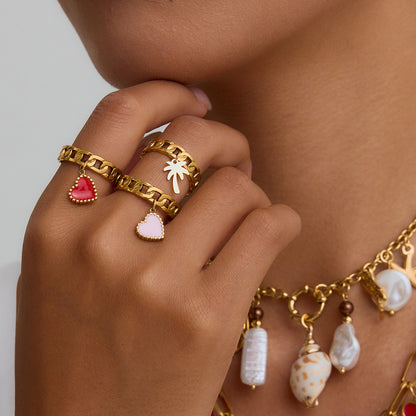 Model hand wearing stackable gold heart rings with white outfit and charm necklace