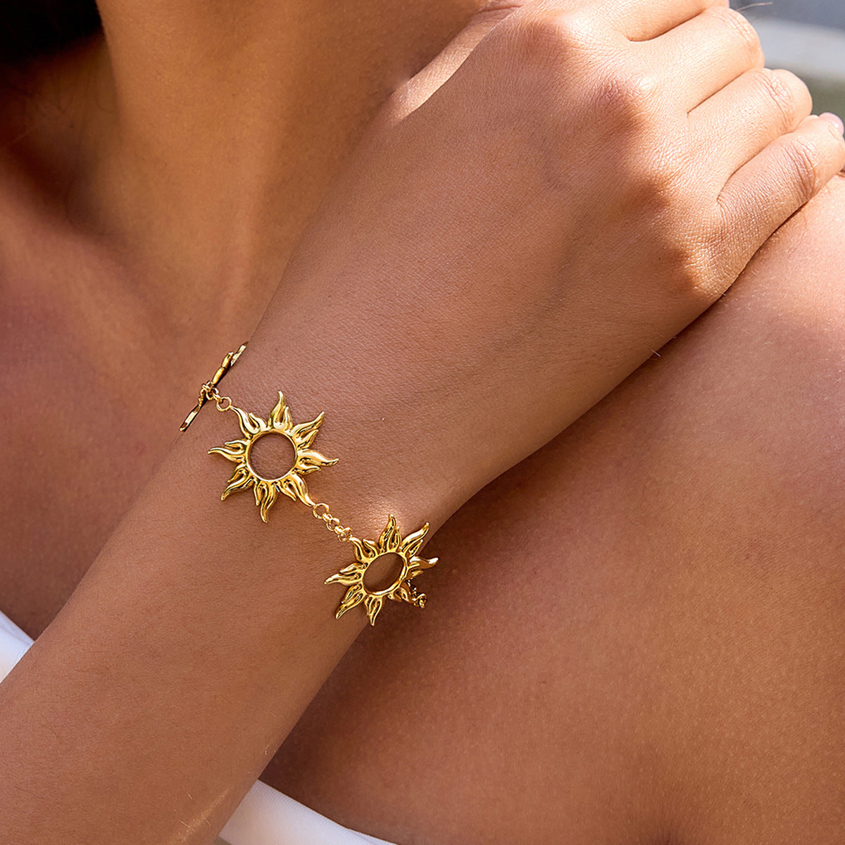 Model touching her shoulder, showing off layered gold sun charm bracelet in sunlight