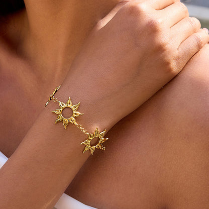 Model touching her shoulder, showing off layered gold sun charm bracelet in sunlight