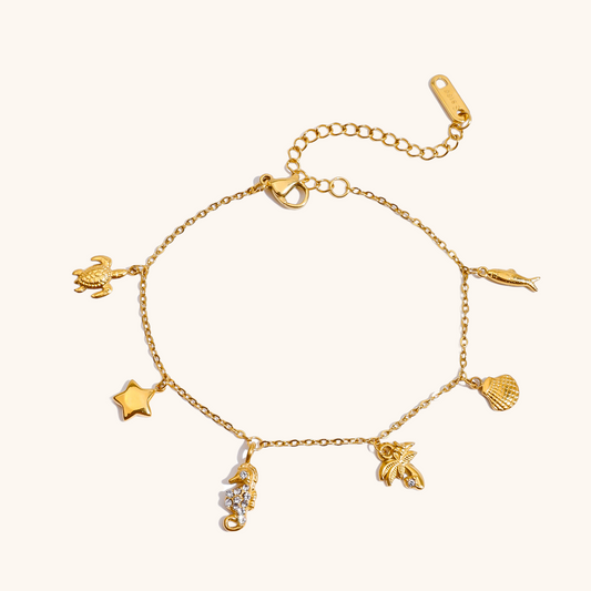 Gold charm bracelet styled on tropical beach sand, featuring ocean-inspired pendants.