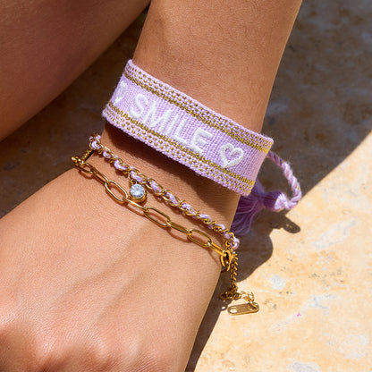 Model by the pool wearing layered bracelets, including purple and gold charm chain
