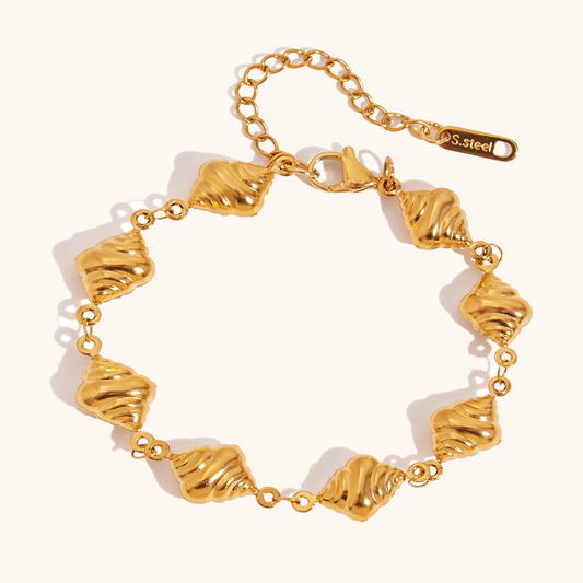 Close-up of gold sun charm and fresh-water pearls on golden brioche bead bracelet laid on white background